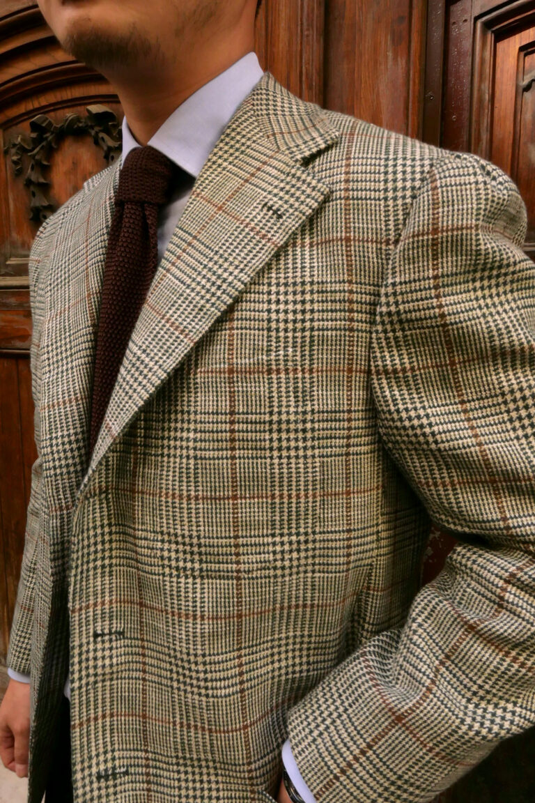 Handmade Neapolitan bespoke sport coat in a beige Prince of Wales check fabric with brown overcheck, featuring soft shoulders, wide lapels and a brown knitted tie.