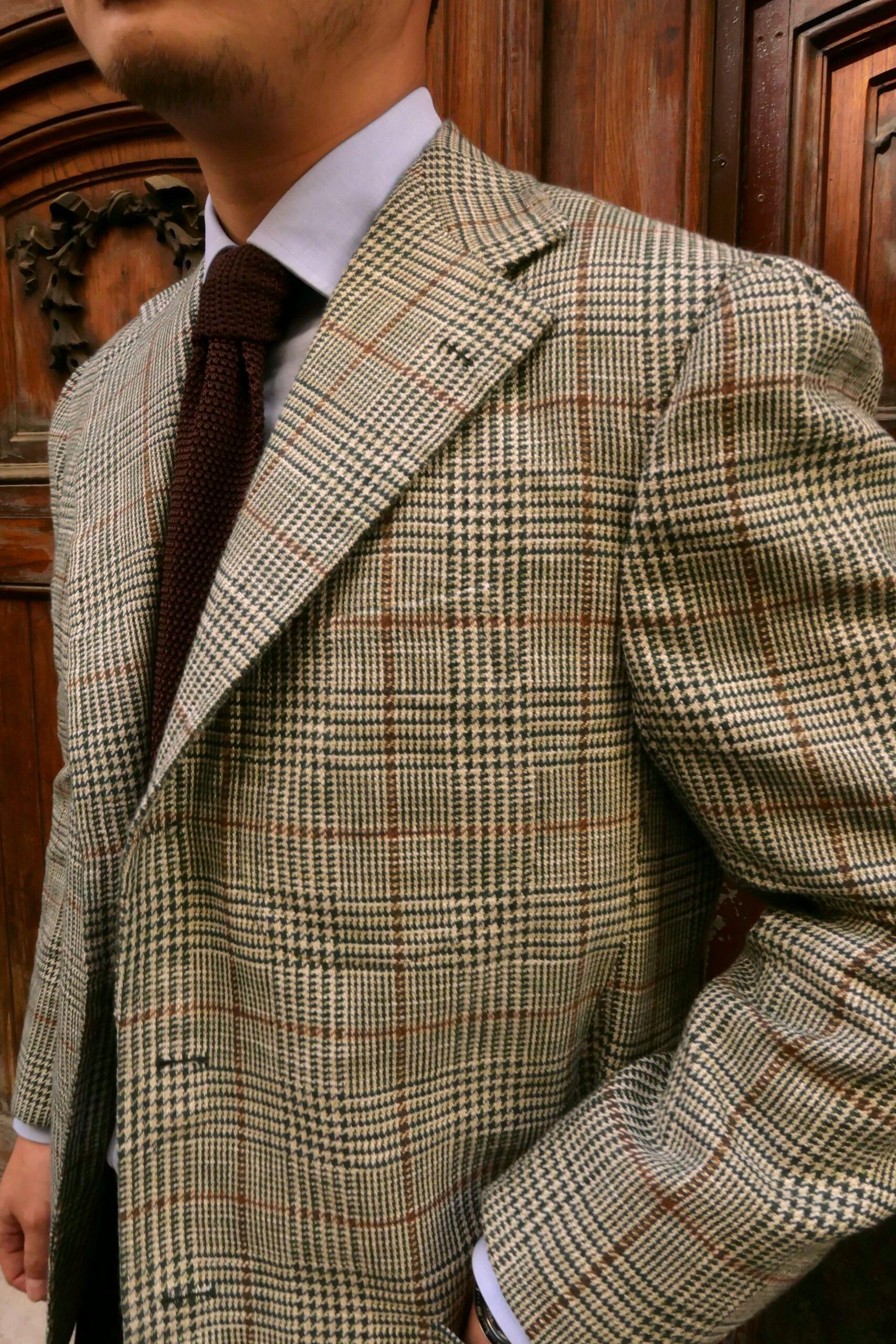 Handmade Neapolitan bespoke sport coat in a beige Prince of Wales check fabric with brown overcheck, featuring soft shoulders, wide lapels and a brown knitted tie.